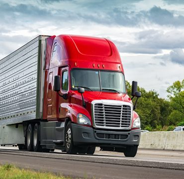 Horizontal shot of a red semi-truck on an interstate highway.